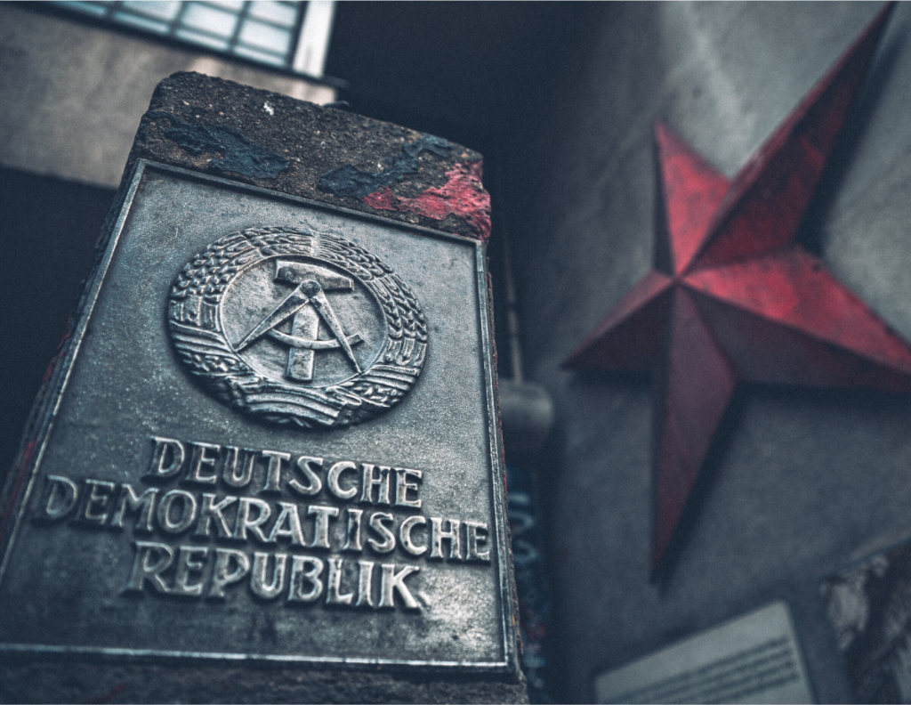 Tirage photo DDR Berlin avec plaque métallique Deutsche Demokratische Republik et étoile rouge, ambiance urbaine grise métal et rouge vintage.