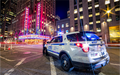 Photo de nuit à New York avec un véhicule du NYPD aux feux allumés au premier plan et le Radio City Music Hall en arrière-plan, ambiance lumineuse urbaine.