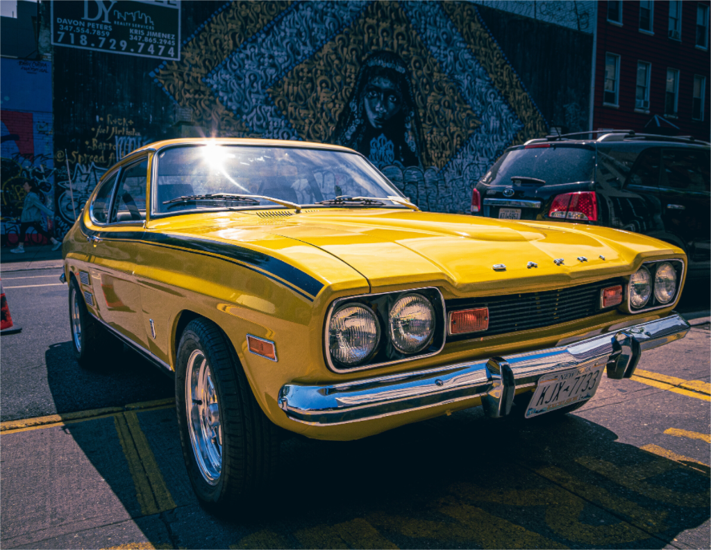 Photo de la Ford Capri 2000 GT jaune vintage dans une rue de New York, ambiance urbaine et rétro.