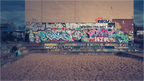 Tirage photo JOE à Berlin avec mur de graffitis variés entre la Spree et East Side Gallery, ambiance urbaine vintage aux couleurs éclatantes.