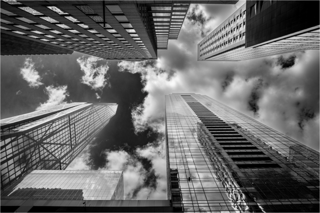 Photo en noir et blanc de quatre gratte-ciels de New York, prise en contre-plongée avec un ciel nuageux, perspective graphique et spectaculaire.