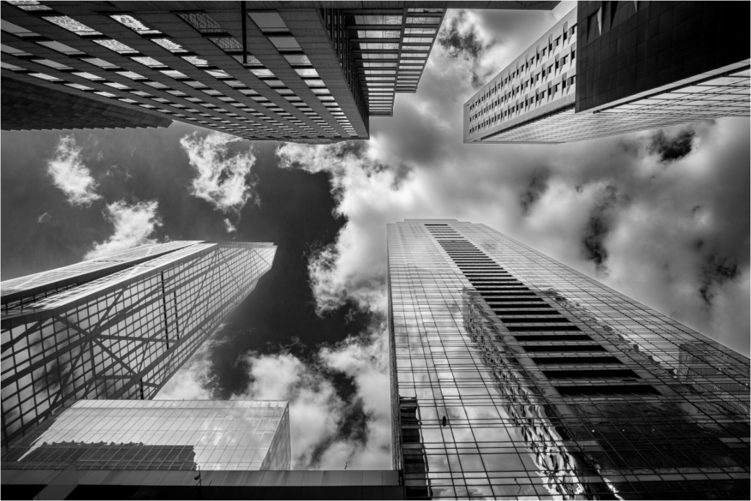 Photo en noir et blanc de quatre gratte-ciels de New York, prise en contre-plongée avec un ciel nuageux, perspective graphique et spectaculaire.