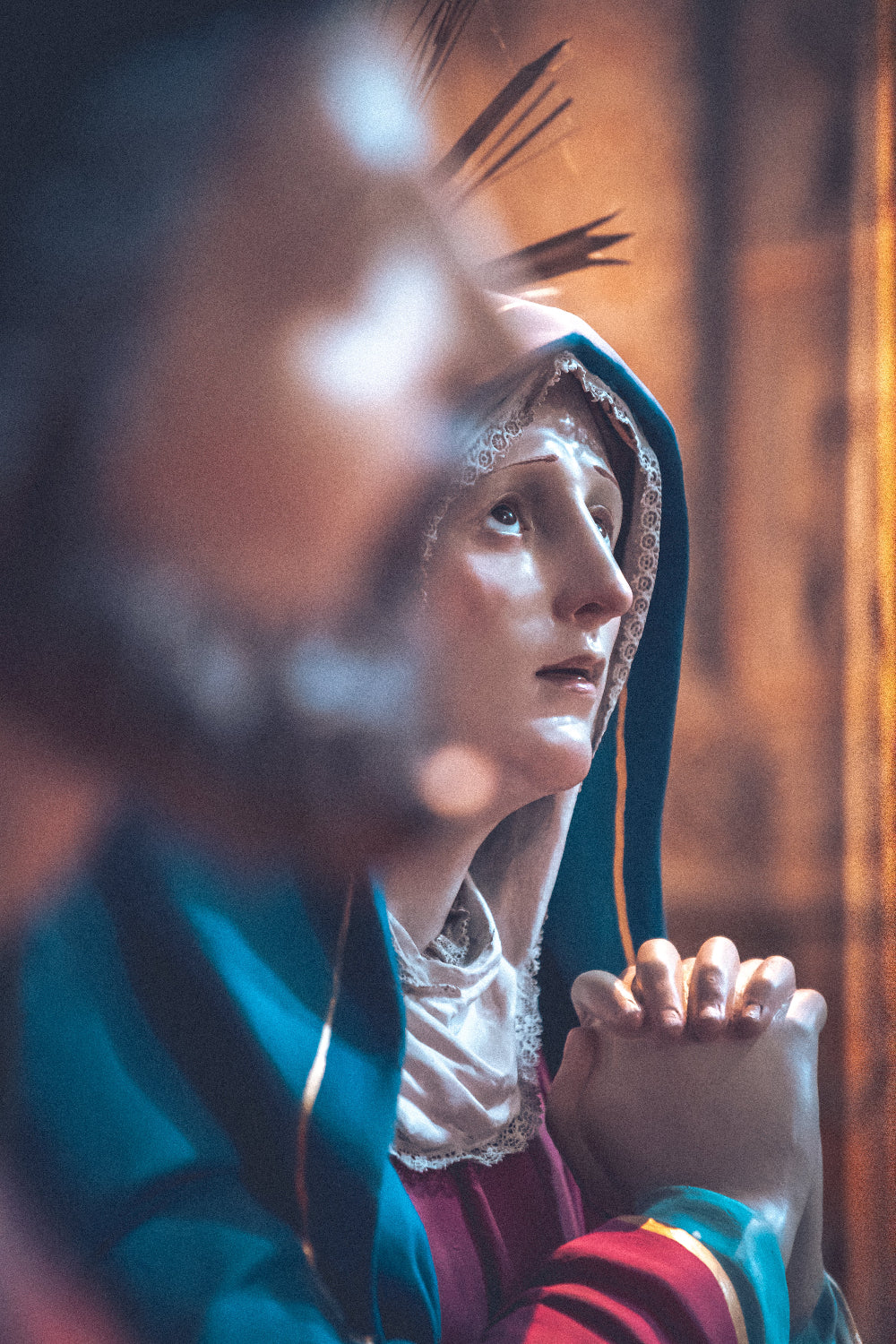 Photo couleur de la Vierge Marie en prière dans une basilique à Lecce, regardant vers le ciel, avec un flou au premier plan laissant apparaître le visage de Jésus