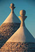Deux toits coniques de trulli au coucher de soleil dans les Pouilles, cadrage serré, ciel bleu et lumière chaude de fin de journée