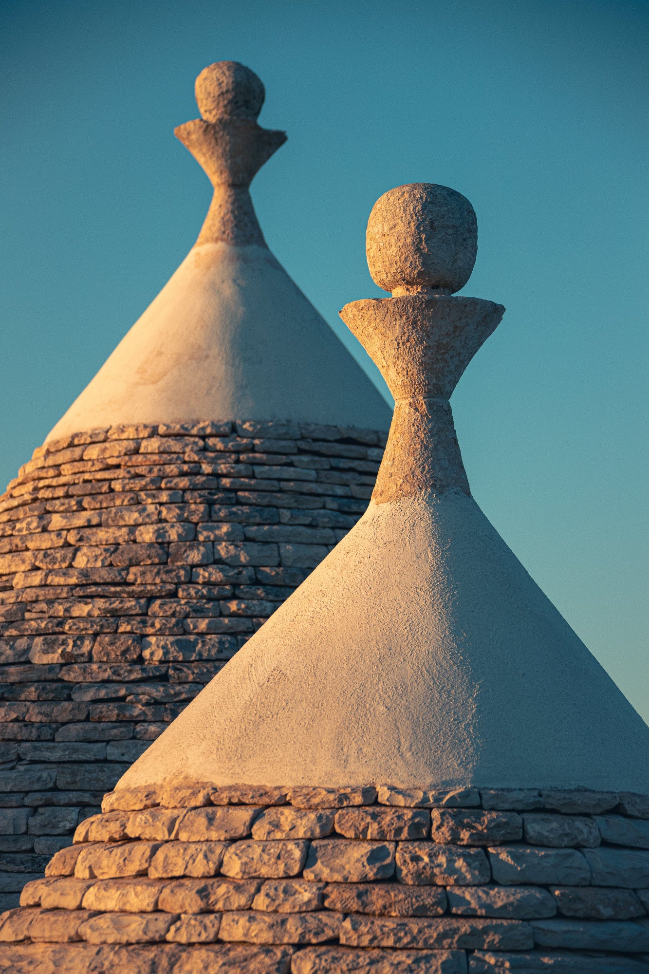 Deux toits coniques de trulli au coucher de soleil dans les Pouilles, cadrage serré, ciel bleu et lumière chaude de fin de journée