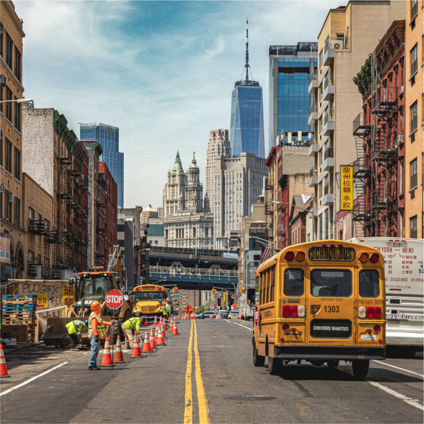 School bus jaune à New York roulant le long de travaux urbains avec un autre bus en attente, buildings en arrière-plan
