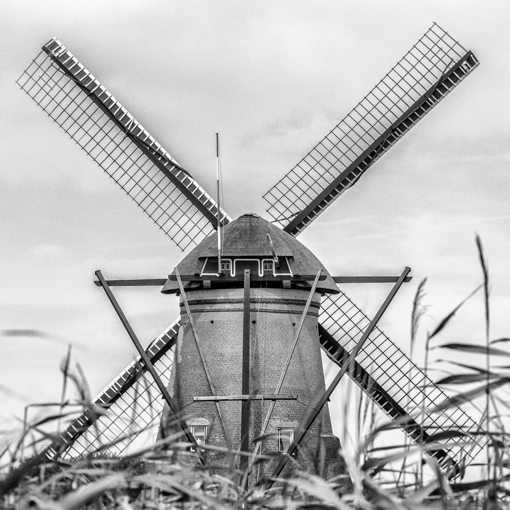 Photo noir et blanc d’un moulin à vent vu de dos à Kinderdijk, dont les quatre pales alignées forment une croix parfaite